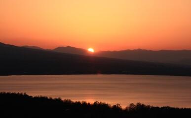 夕暮れの山中湖　　山中湖のの向こうに見える南アルプスに沈むオレンジ色の夕日