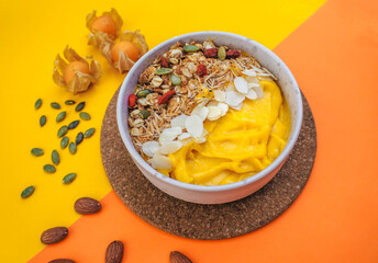 mango smoothie bowls with fruits, nuts, seeds and granola for healthy on color paper background with empty space for your text or message.