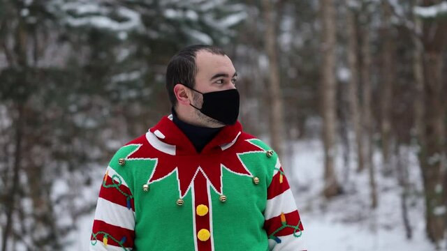 portrait of a young man in a Christmas sweater, wearing a mask, looks around, in the middle of the forest.