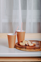 Heart-shaped cookies on round wooden cutting board. Saint Valentine's cookies in shape of heart and craft coffee cups on white background. Two paper coffee to go with tubes.