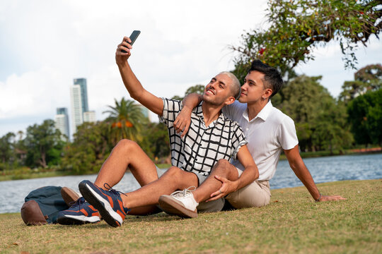 Young gay couple taking selfies a public park
