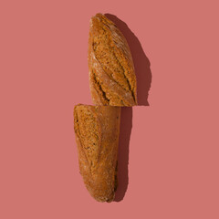 Loaf of bread cut in half on a pastel pink background. Minimal aesthetic flat lay.