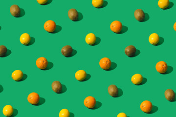 Lemons, oranges and kiwis creative pattern on a green background. Minimal sunlit layout.