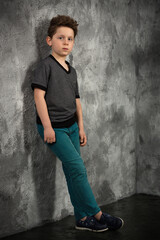 teen boy in gray t-shirt and blue pants posing against an old wall with plaster