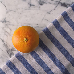 Orange fruit on a blue and white striped cloth with white marble background. Minimal food arrangement.