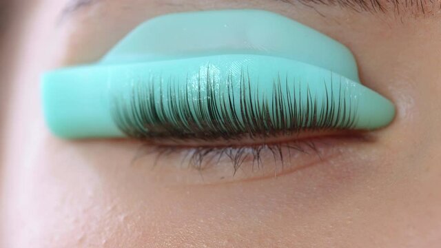 Face of a young girl before a modern eyelash lamination procedure in a professional beauty salon. The master applies special glue before the eyelash curling procedure close up.