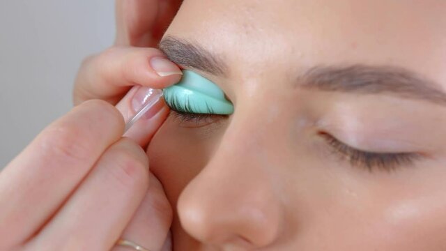 Face of a young girl in a modern eyelash lamination procedure in a professional beauty salon. Master apply black dye paint to the eyelashes during the eyelash curling procedure with a special brush.