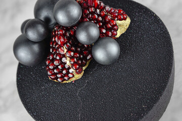 Fancy black cake decorated with chocolate spheres and two pieces of ripe pomegranate. Chocolate birthday cake.