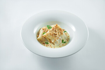 A dish of Ukrainian cuisine - pancakes stuffed with applw with sweet creamy sauce on a white plate on a white plate. Blini or french crepes