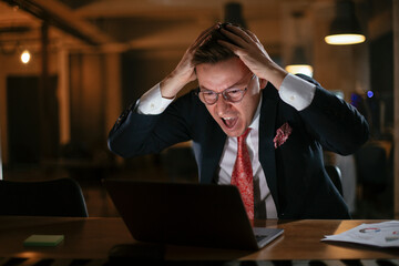 Young businessman working with laptop at office. Tired man sitting at office desk working on laptop computer..