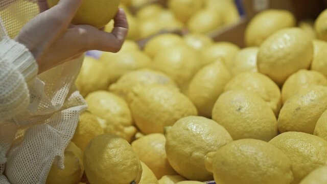 Woman's hand lays lemons in string bag. Close-up. Shop with this environmentally friendly string bag.