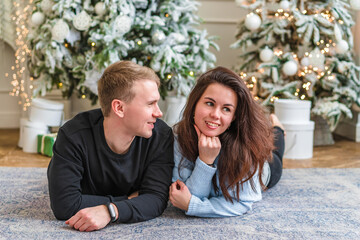 Beautiful young couple man and woman lying on the living room floor next to a nicely decorated Christmas tree and talk