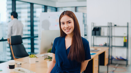 Portrait of successful beautiful executive businesswoman smart casual wear looking at camera and smiling, happy in modern office workplace. Young Asia lady standing relax in contemporary meeting room.