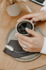 Cup of black coffee  on wooden table in woman hands. Hipster traveler girl in the morning sun day, mockup