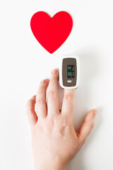 Covid Valentine day concept, hand with pulse oximeter on a finger and a heart symbol on white background
