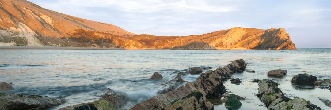 Panorama view of shoreline at Lulworth cove in Dorset with cliffs in the background