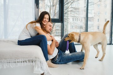 Young beautiful couple with dog sitting on the floor at new home.