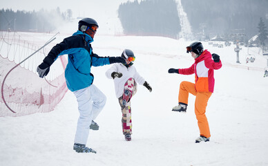 Group of friends wearing vivid ski suits warming up before skiing from piste in mountains in...