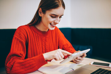 Cheerful female freelancer using tablet for work in cafeteria