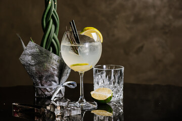 Transparent alcohol cocktail with lime and ice on the dark background