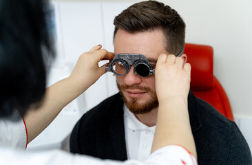 Male patient in ophthalmology clinic. Trial frame on handsome man`s eyes. Health check up in...