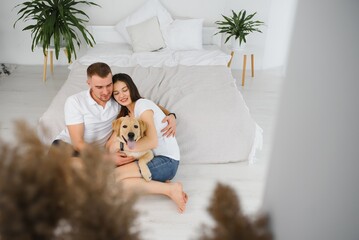 Young couple with a dog at home. Young man and a woman playing at home with dog.