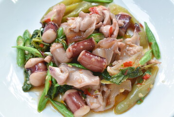 spicy fried chili squid with slice yard long bean and basil leaf on plate