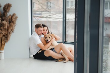 Happy Loving Family Concept. Portrait of beautiful couple with dog sitting on the floor in modern apartment