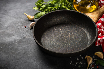 Food cooking background with Frying pan or skillet, spices, herbs and olive oil on black stone table. Top view with copy space.