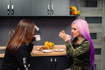 Young modern girls communicate at home in the kitchen with a cup of coffee. The pastime of girlfriends.