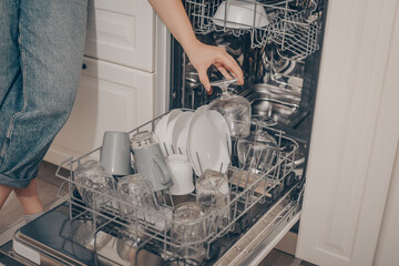 Built-in dishwasher, dishwashing. A woman loads washed dishes, cups, glasses. A woman's tender hand puts a glass goblet in the dishwasher or pulls out, unloads.