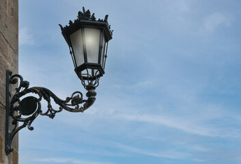 Fototapeta na wymiar iron street lamp lit with blue sky background