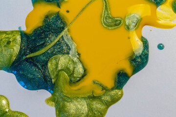 Background of spilled nail Polish in yellow, green, blue colors with sequins.