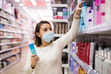 Young woman in mask choosing hair care products at shop