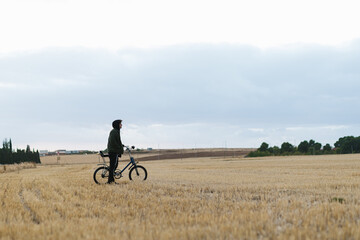 Young man with his vintage bicycle observing a dry field in the countryside
