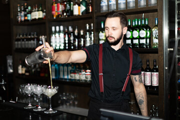 Bartender making refreshing coctail on a bar background. Dark moody style. Ice in the glass. Fosuc on model