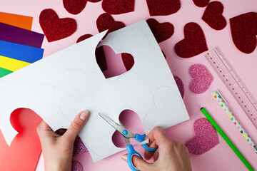Woman's hand holds a scissors and cuts a hearts from paper. DIY concept for Valentine's day card crafts. Top view. Flat lay. Step by step photo instruction. Step 4.