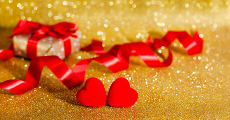 Two red hearts and gift box on glitter golden background. Concept of congratulations for Valentine's day. Holiday gift. Banner. Place for text.