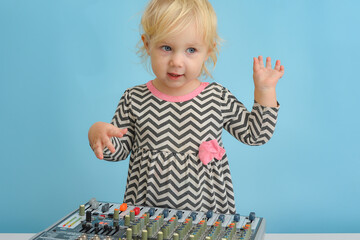 A little funny and cheerful girl stands near the music mixing console and waving her arms.