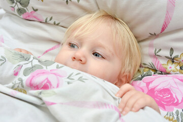 A little girl with open eyes lies in a children's bed.