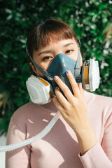 Beautiful asian thai woman in pink shirt wearing respirator gas mask for breathing during covid-19...