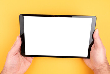 close-up view of hands holding tablet computer with copy space on screen against orange colored background