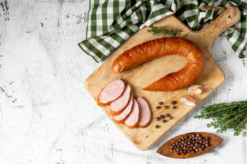 Smoked Cracow sausage on a wooden serving board on a light gray kitchen table. Slicing boiled and smoked sausage
