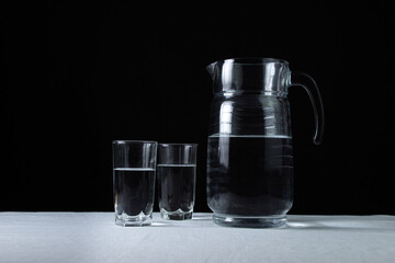 Decanter with water on a black background. A decanter and two glasses filled with water. Clean drinking water. Ecology cleanliness concept.