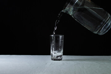Decanter with water on a black background. The decanter fills a glass with water. Clean drinking water. Ecology cleanliness concept.