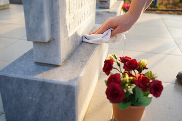 Cleaning cemetery. A woman's hand washes grey monument at the grave with rag