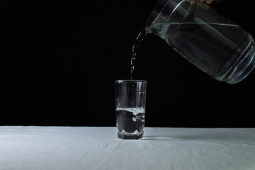 Decanter with water on a black background. The decanter fills a glass with water. Clean drinking water. Ecology cleanliness concept.