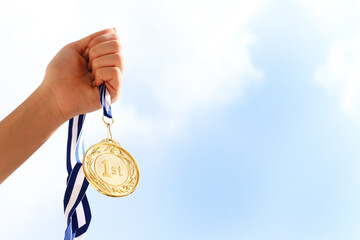 Fototapeta na wymiar woman hand raised, holding gold medal against sky. award and victory concept