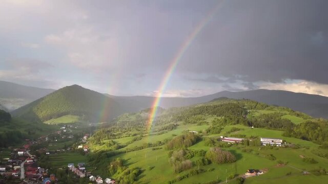 Aerial view of double rainbow above green country landscape in summer evening with rain and sun light