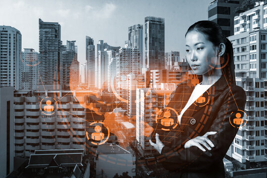 Attractive young Asian HR director at international company is thinking about recruitment of highly qualified specialists. Women in business concept. Social media hologram icons over Bangkok. - Powered by Adobe